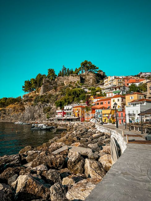 A scenic Greek hill village overlooking the sea, with stone buildings and a harbor below.