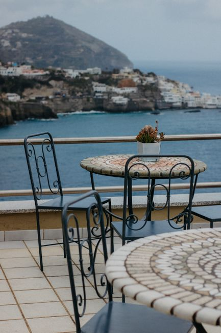 A quiet hillside boutique hotel terrace overlooking the sea at sunset, with a calm elevated view above the coast.
