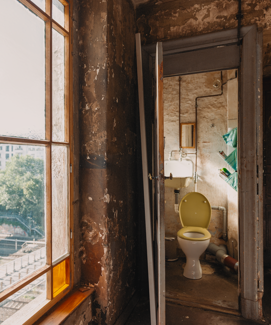 Bathroom under renovation with walls opened and plumbing exposed behind the fixtures.