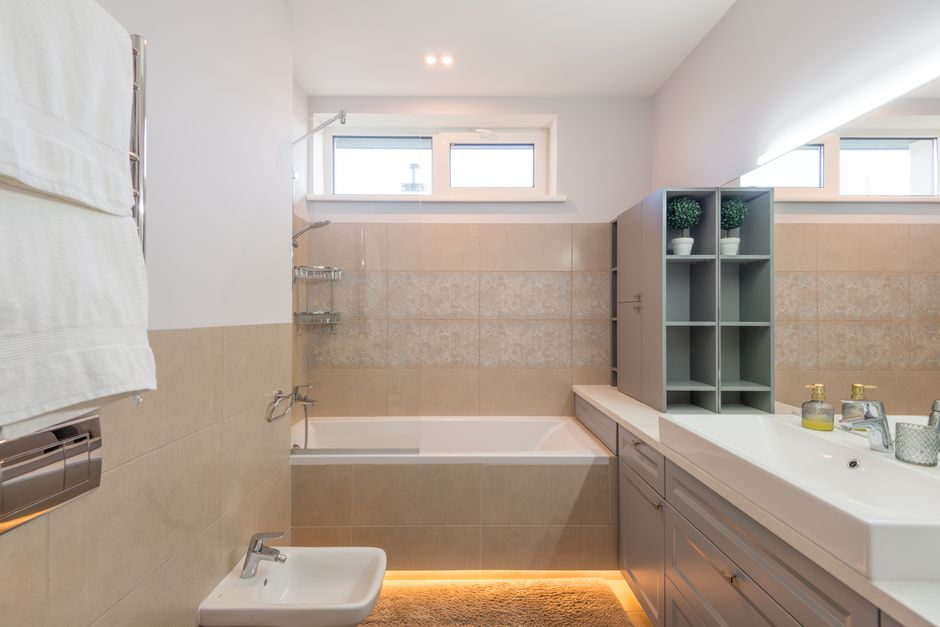 A homeowner or inspector checking a damp bathroom or under-sink area with a flashlight for moisture clues.