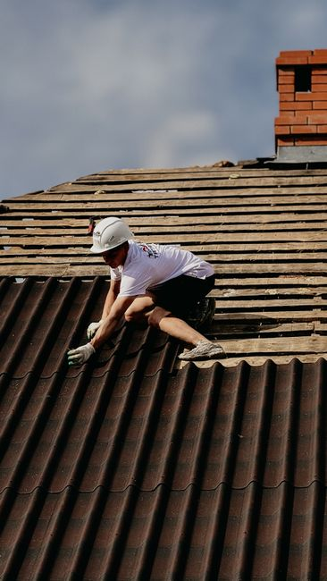 Roofing crew removing old roofing material from a residential home while debris is collected below.