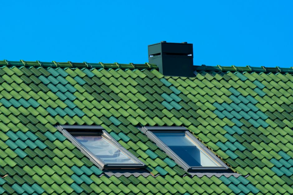 A roofing worker cleaning up around a home after installation, with a finished roof visible above.