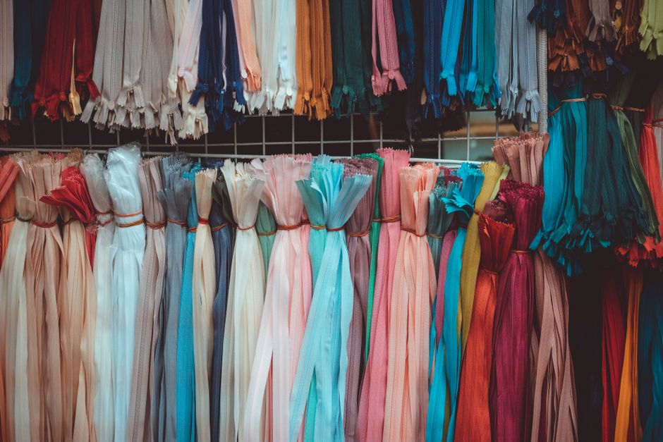 Rows of fabric bolts and folded textiles in a fabric store or sewing studio.