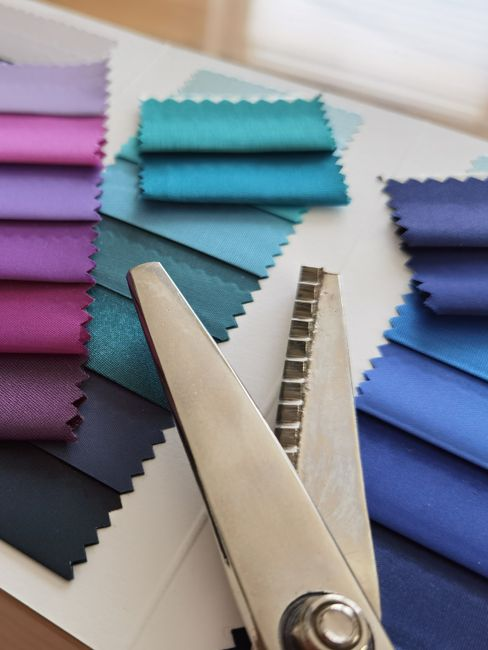 Assorted fabric swatches and textile samples laid out on a table with a measuring tape for comparison.