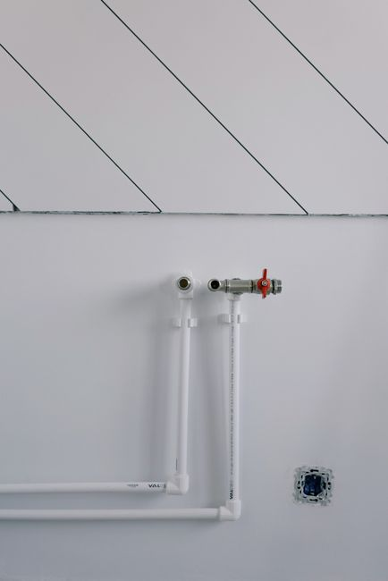 A bathroom under renovation with wall sections open, showing exposed plumbing and construction work behind finished surfaces.