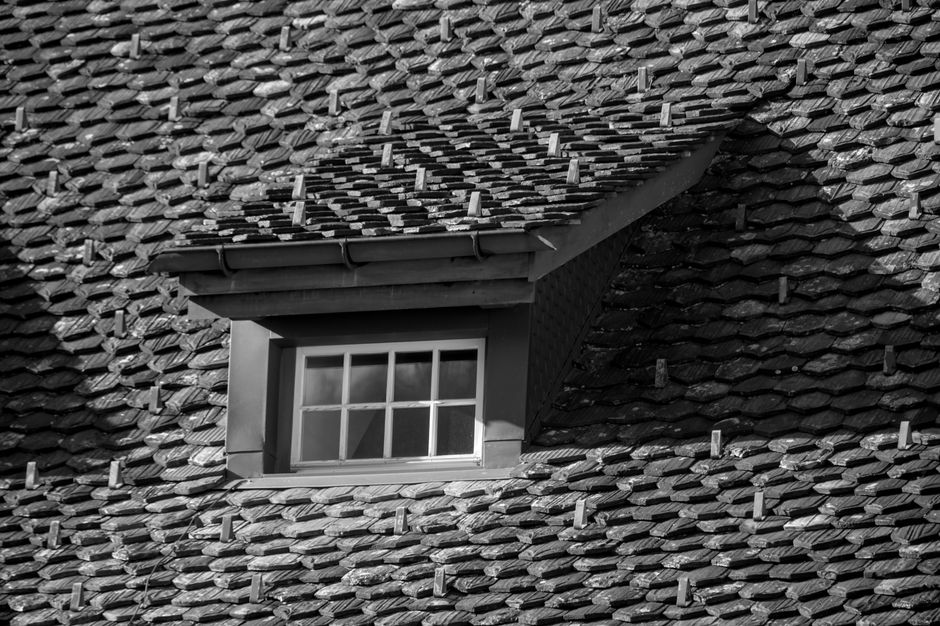 Ground-level view of a house roof with several lifted or displaced shingles or tiles.