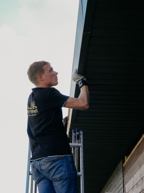 A technician on a ladder inspecting a home's roofline and exterior entry points.