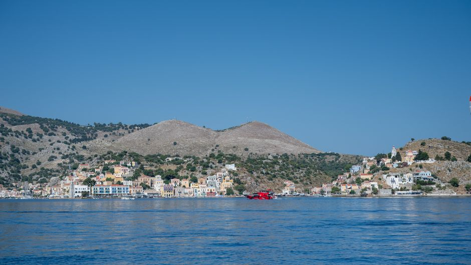 A calm coastal village on Lesbos with blue water, hillside buildings, and a quiet harbor.