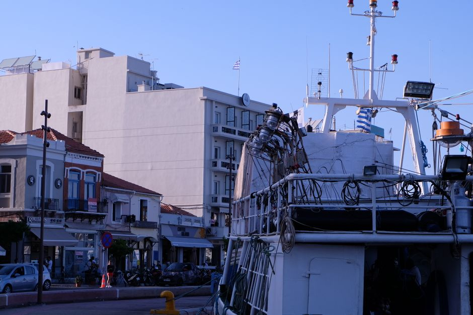 A lively Greek harbor town with waterfront buildings, boats, and a busy promenade.