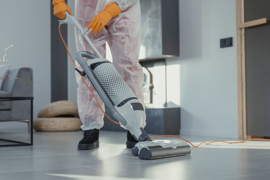 Small rodent droppings gathered along a baseboard in a garage while a gloved hand inspects the area.
