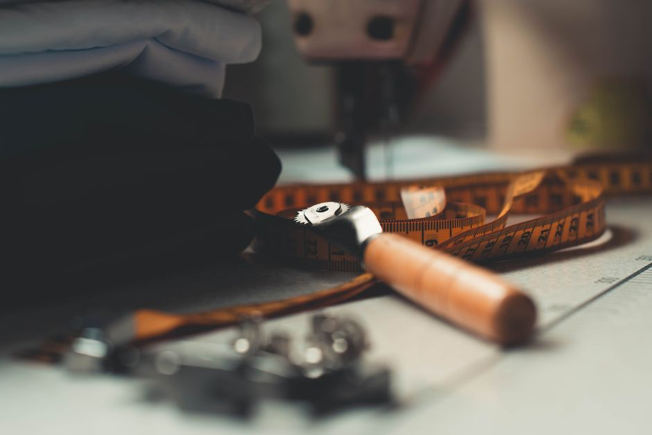A sewing workspace with knit fabric feeding under a sewing machine beside fabric shears and pattern pieces.