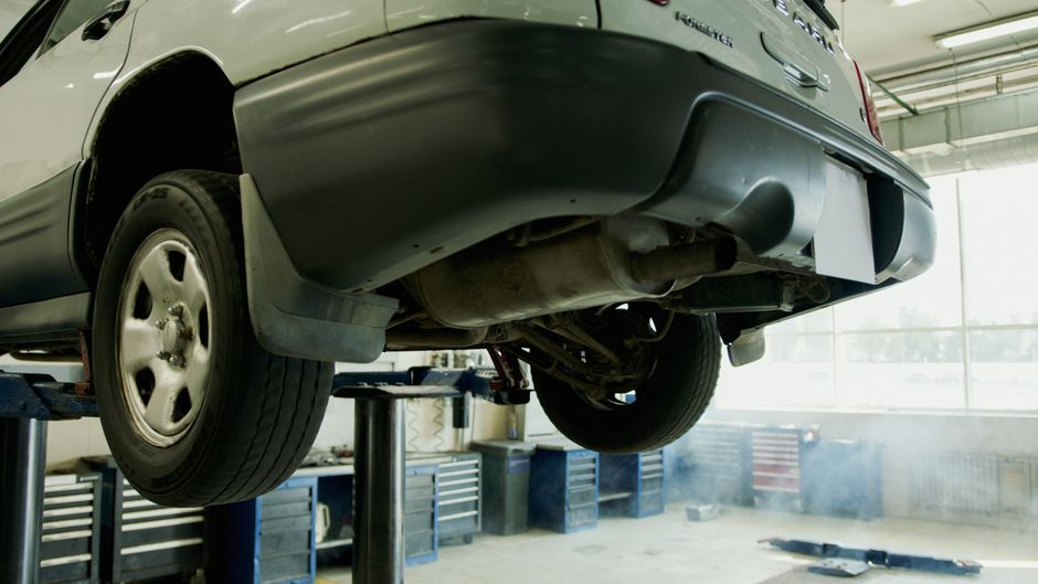 A vehicle being inspected in a dealership service department with a mechanic nearby.