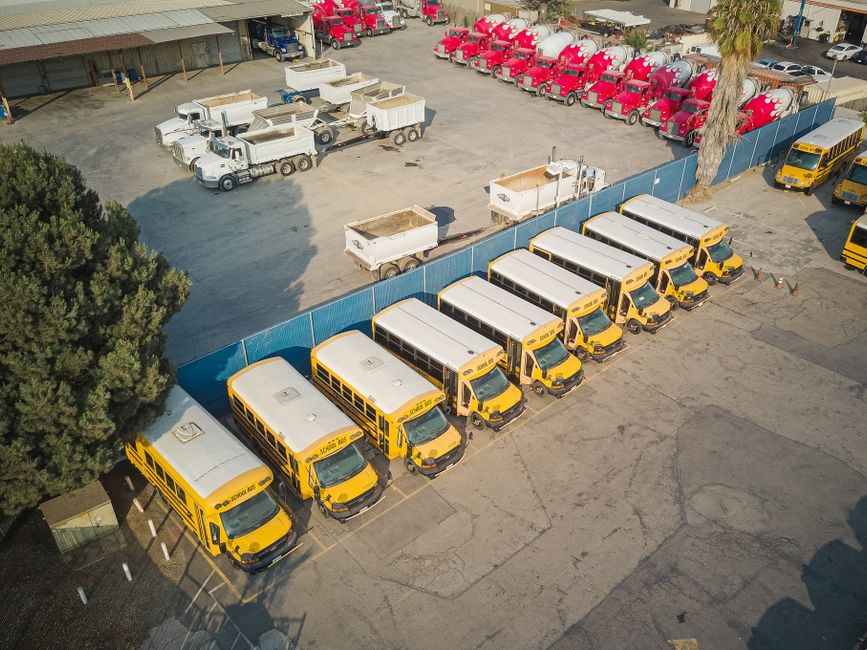 A fleet manager standing near several commercial vans or trucks lined up in a parking area.