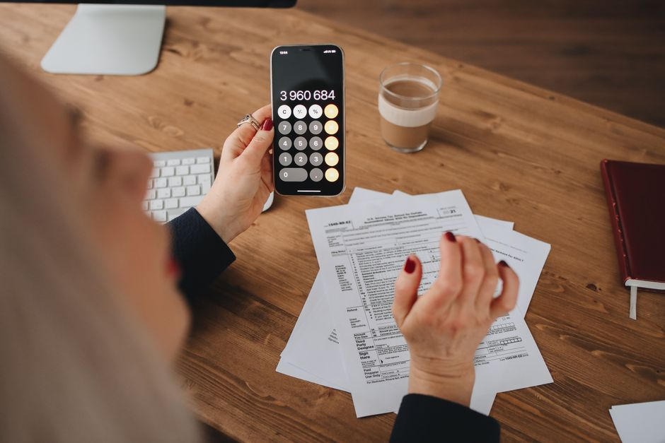 A small business owner reviewing paperwork and financial notes at a desk with a calculator.
