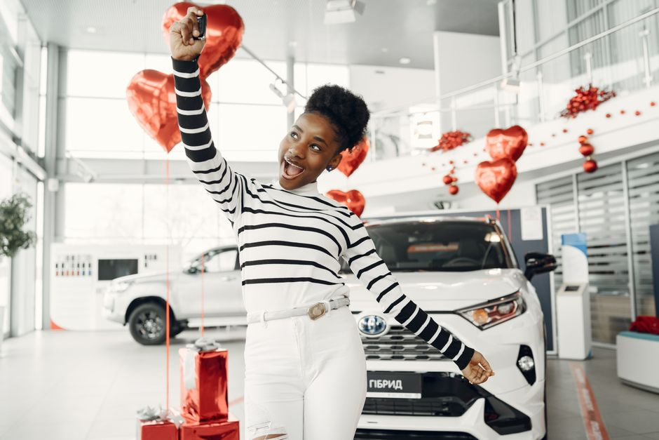 A buyer holding newly received car keys beside a recently purchased vehicle at a dealership.