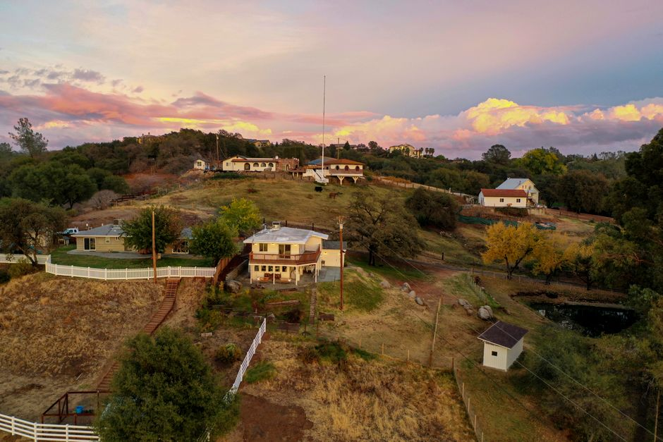 A hillside residential property with mature trees and a sloped yard near the home.