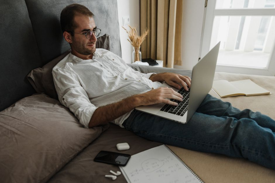 A spare bedroom set up as a simple home office with a desk, laptop, and a few moving boxes nearby.
