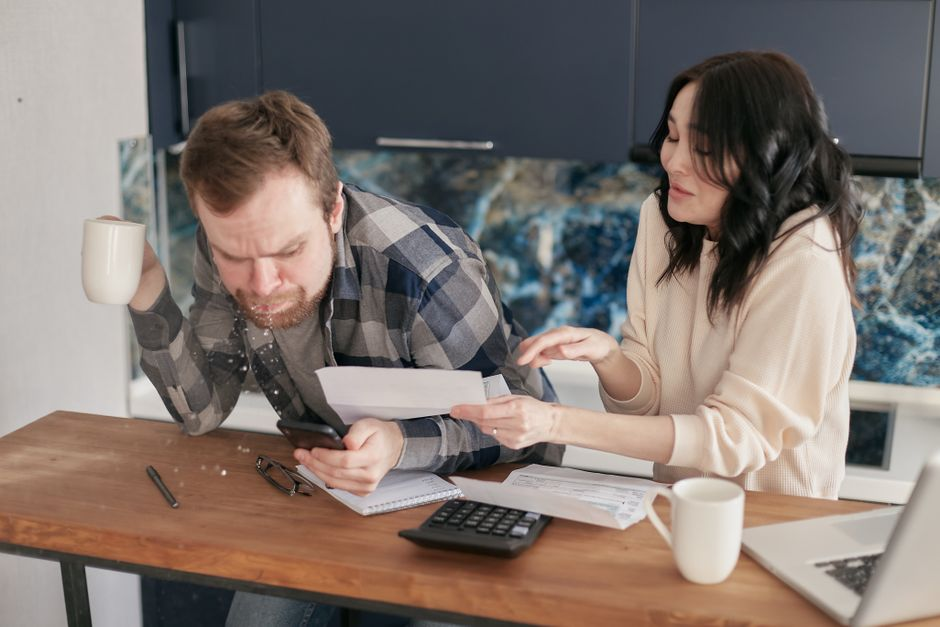Two adults review household financial documents together at a kitchen table.