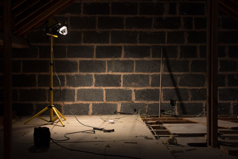 A person inspecting an attic with a flashlight near rafters and roof framing.