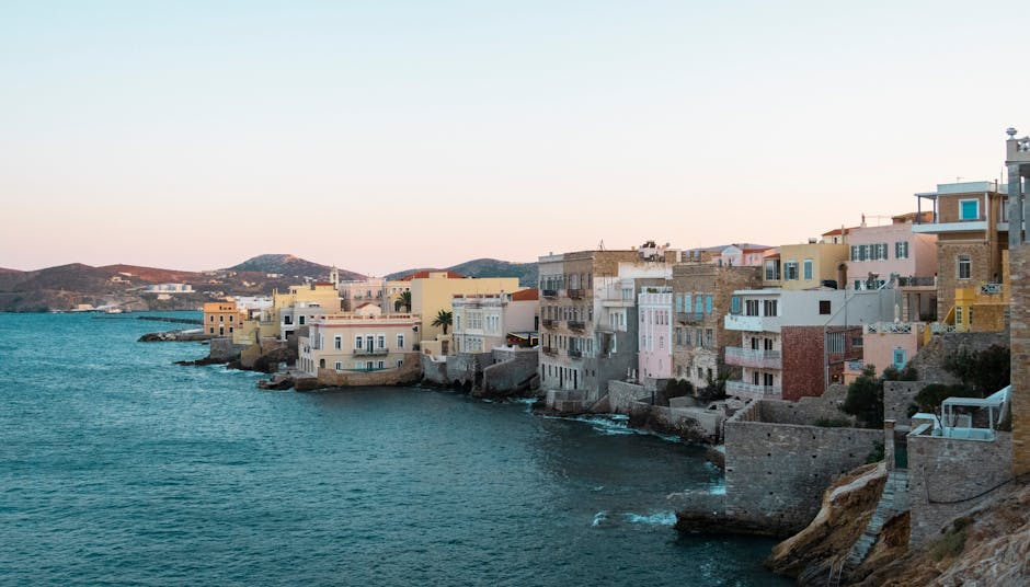 A calm coastal view on a Greek island with blue water, low-rise village buildings, and an unhurried atmosphere.
