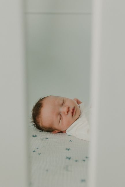 A bedside bassinet positioned next to an adult bed in a calm, compact bedroom.
