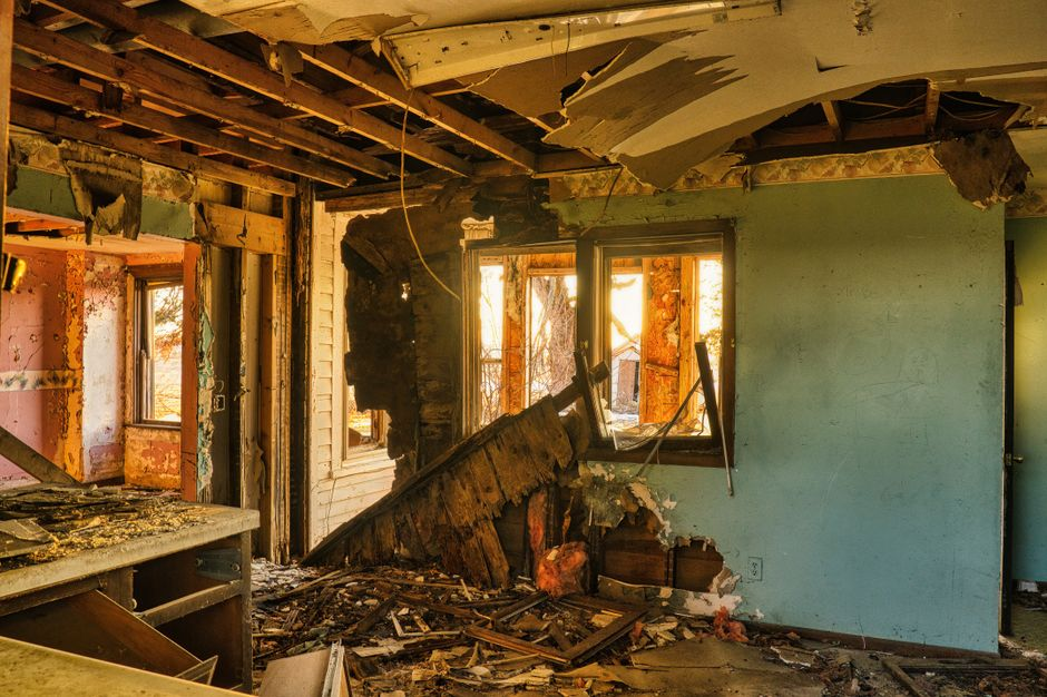 A homeowner standing in a smoke-damaged kitchen taking photos of fire and soot damage with a phone.
