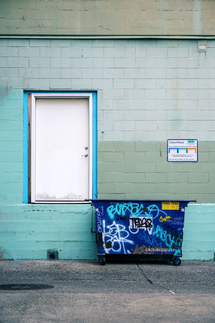 Exterior view of a commercial loading dock beside a dumpster enclosure at a warehouse facility.