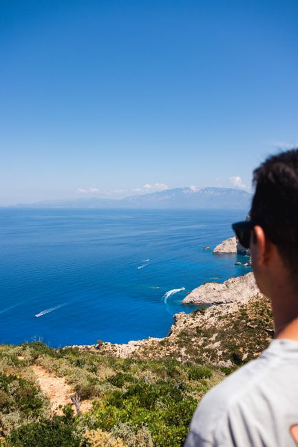 Mavi Ege denizi ve yamaçtaki yapılarla bir Yunan adası kıyısının geniş görünümü.