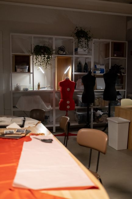 A dressmaking workspace with satin swatches, measuring tools, and pattern materials laid out on a table.