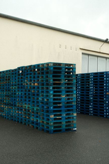 Rows of palletized goods and storage racks in a warehouse, showing wall edges and inspection visibility around stored materials.