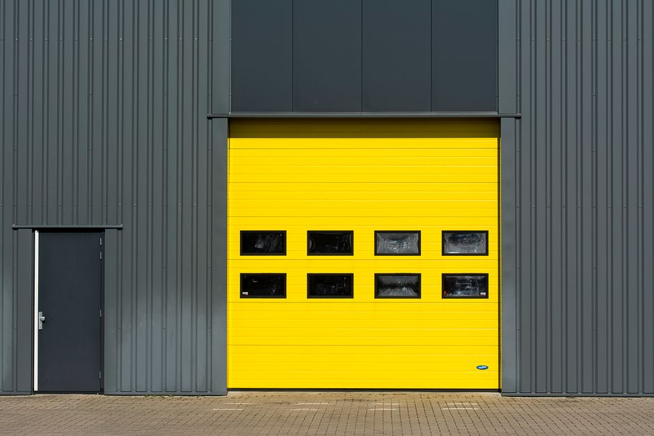 A facility worker inspecting a door threshold and exterior utility entry points on an industrial building.