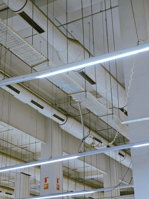 An overhead commercial ceiling area with open tiles exposing utilities and service pathways.