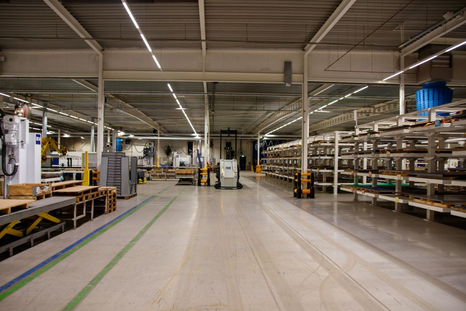 A warehouse or factory interior showing narrow utility-lined service corridors and equipment aisles.