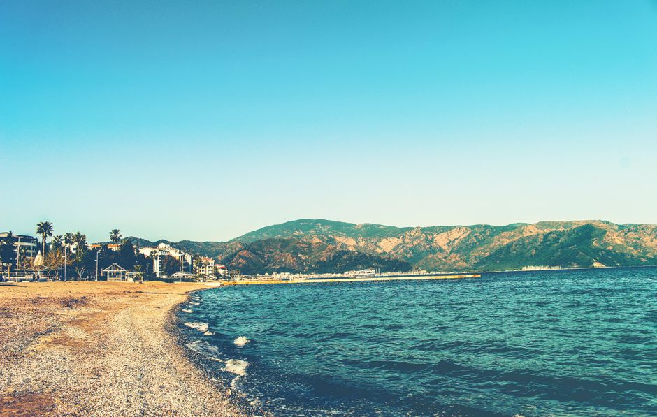 A bright pebble beach with clear blue water and an easy, well-serviced shoreline on a Greek island.