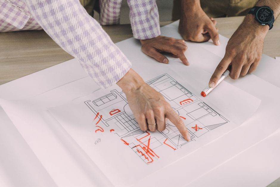 Early custom home sketches and blueprints spread across a table during a planning discussion.