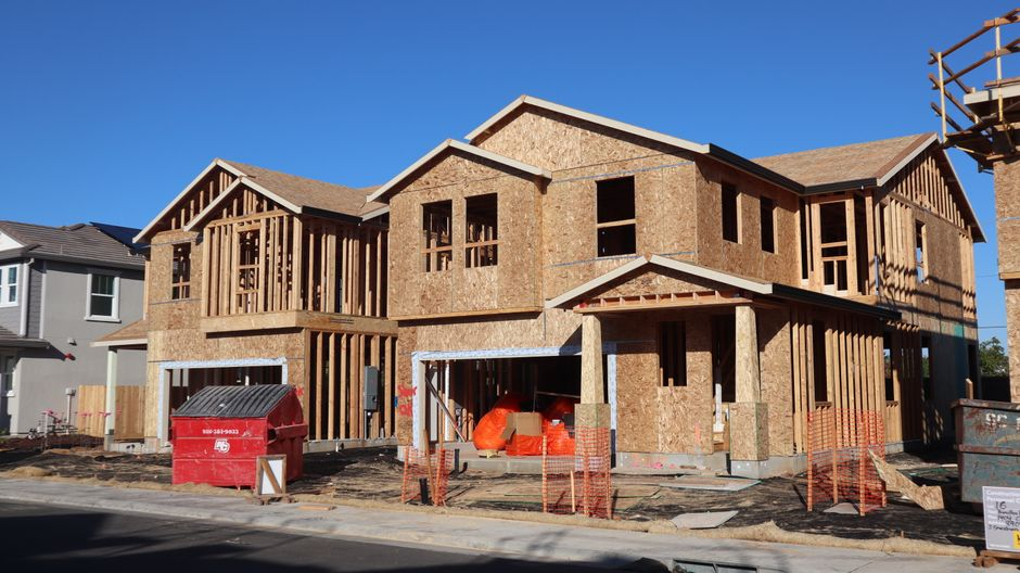 A builder walking an active custom home construction site with framing and materials visible.