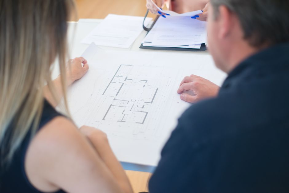A homeowner and design professional reviewing site plans and construction drawings together at a table.
